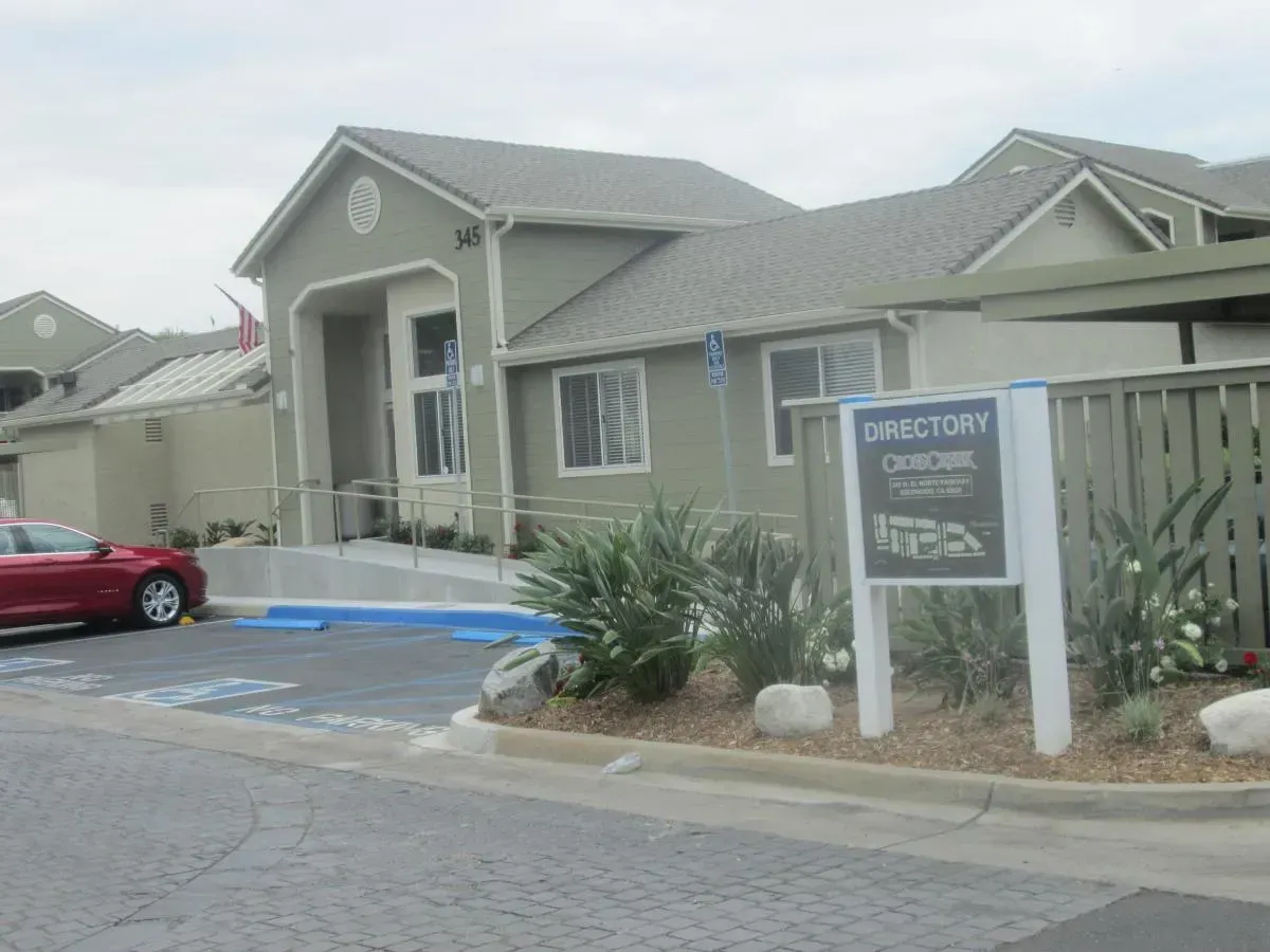 Apartment building entrance with a sign, ramp, and parked red car on a cloudy day
