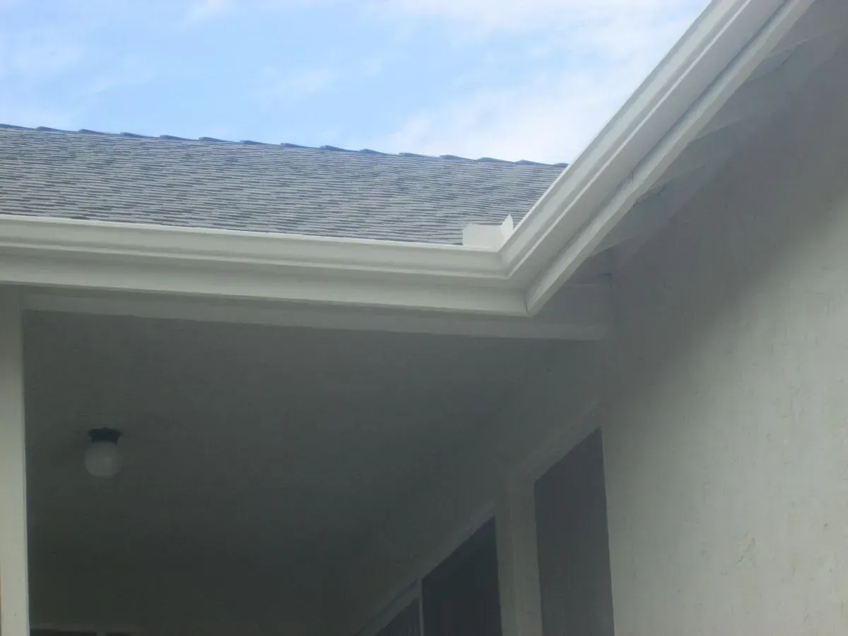 Close-up of a house roof eave and gray stucco wall under a blue sky