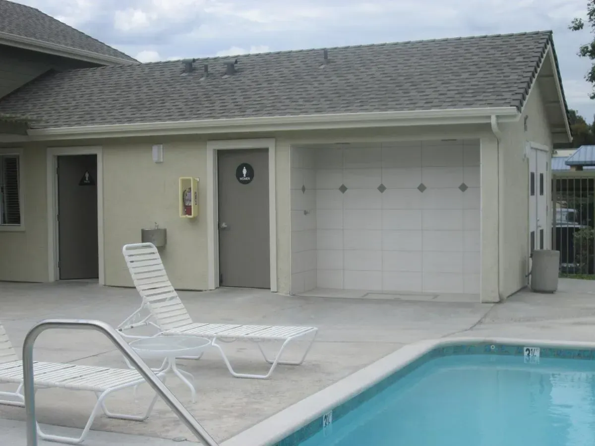 Poolside patio with white lounge chair, beige house wall, garage door, and swimming pool.
