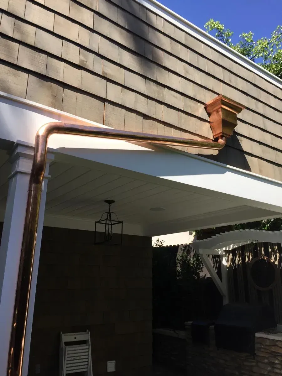 Close-up of a house roof corner with copper gutter and downspout over a patio area