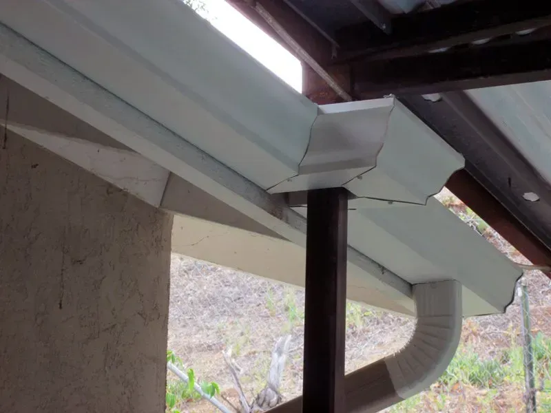 White roof gutter with downspout and black support post under a house eave
