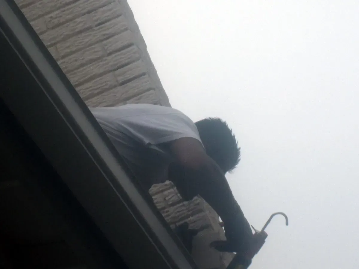 Person reaching up on a balcony with a hook tool against a cloudy sky