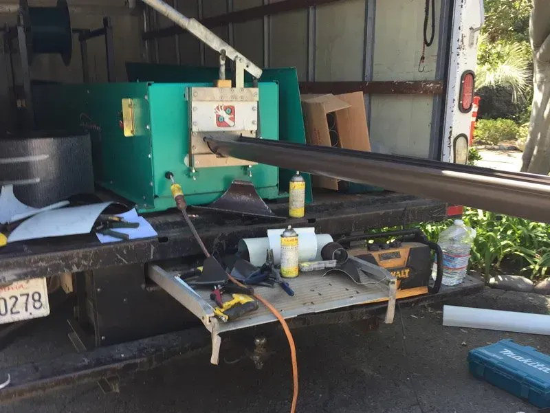 Green portable machine in a garage with long black beams extending from it, tools and hoses nearby.