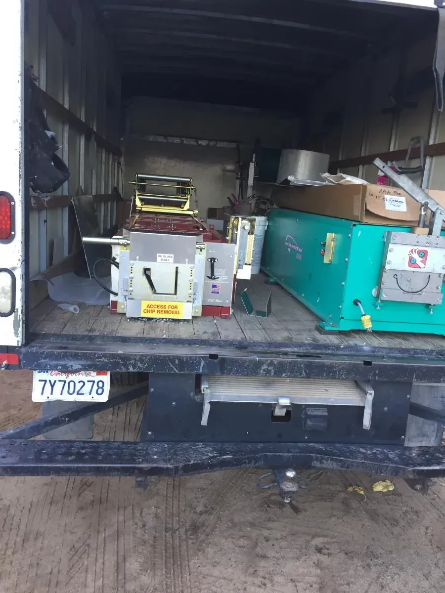 Pickup truck bed loaded with equipment, including green and white machinery and boxes, in a garage or warehouse.