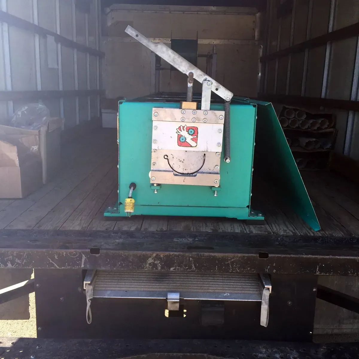 Green industrial machine inside a truck or trailer, with a white top lever and side panel.