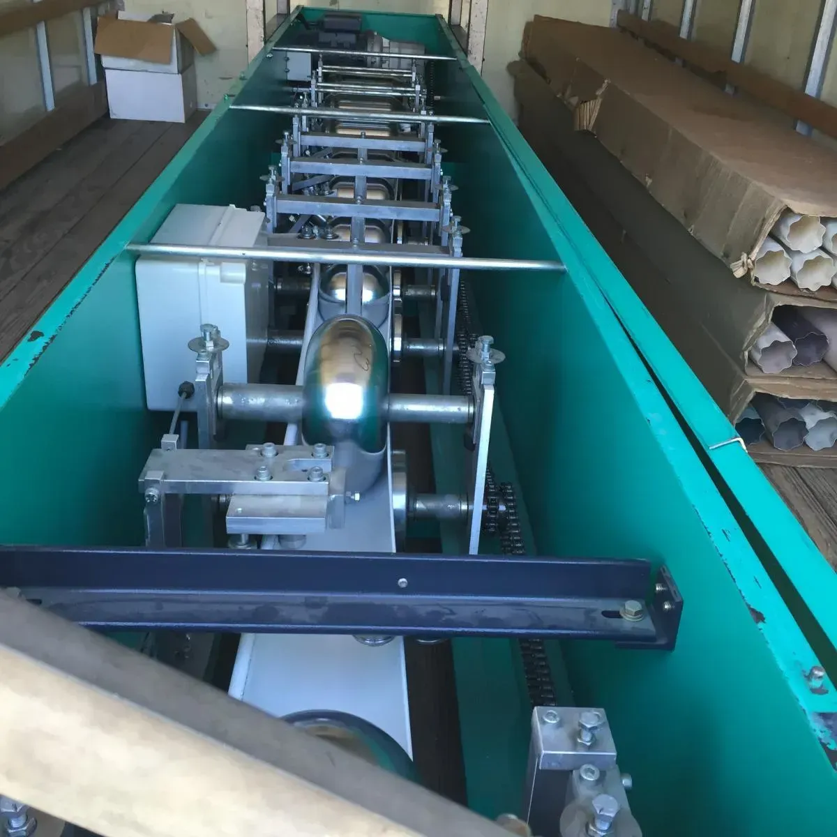 Industrial machine assembly inside a teal shipping crate, with metal components and cardboard packing around it.