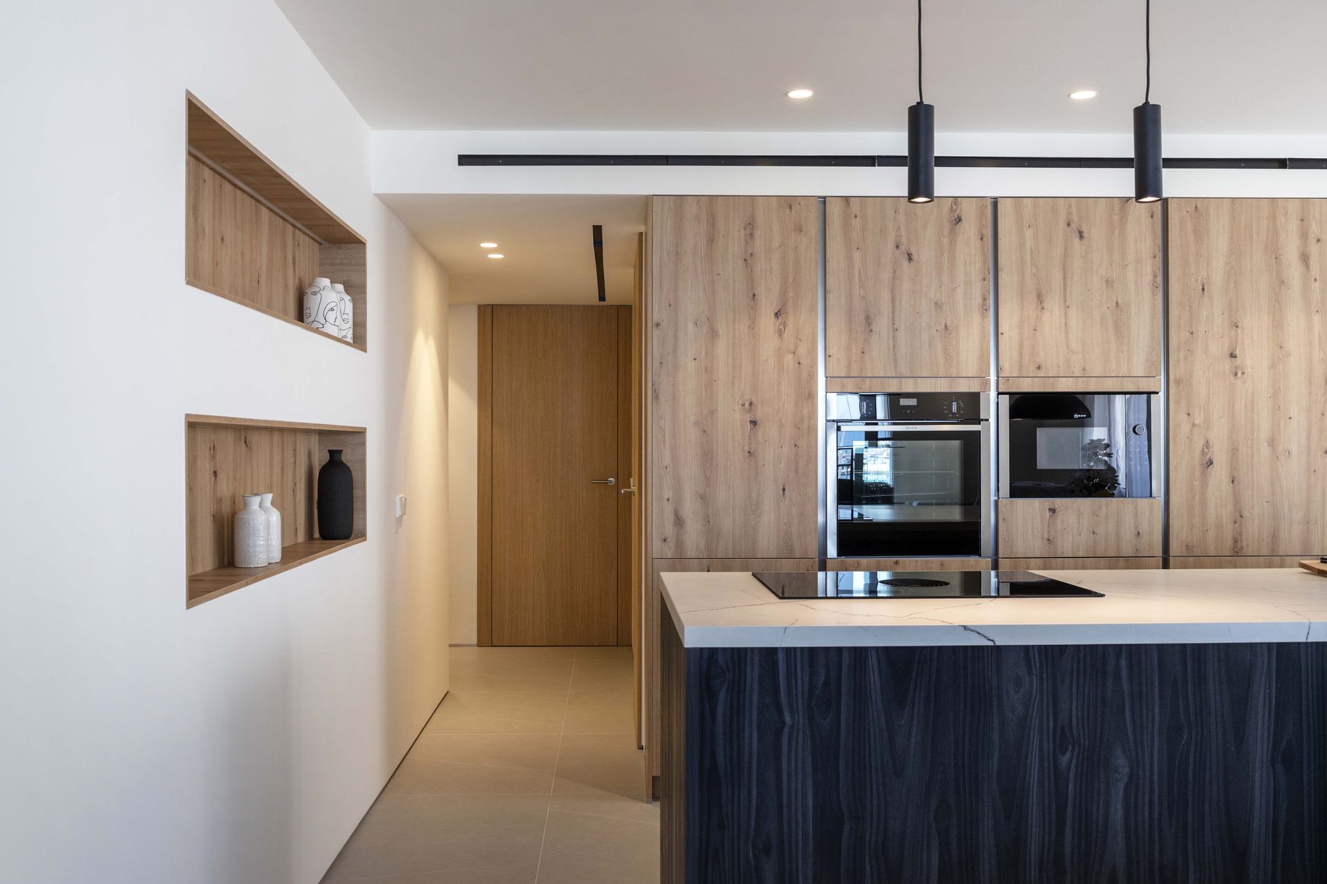 Cocina moderna con gabinetes de madera, hornos empotrados y una isla de cocina clara.