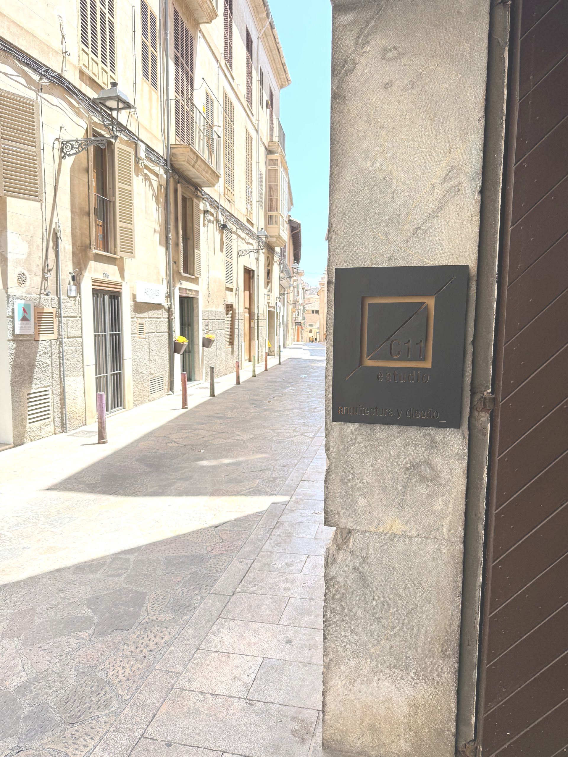 Un estrecho callejón soleado con edificios de piedra y un panel de intercomunicación oscuro en la pared derecha.