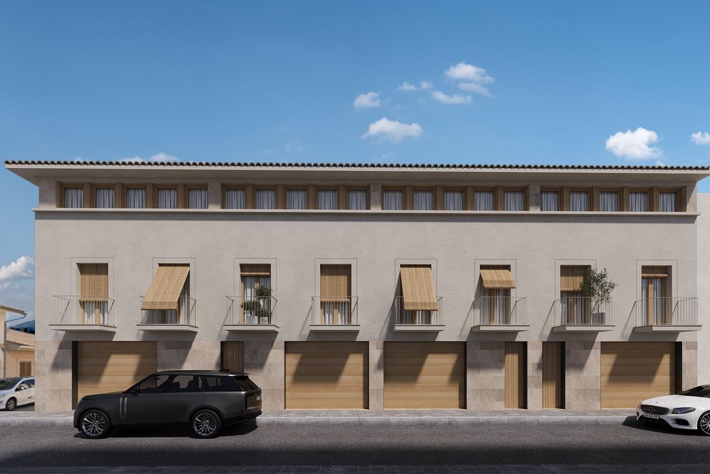 Edificio beige de dos plantas con puertas de garaje y coches aparcados en una calle soleada.