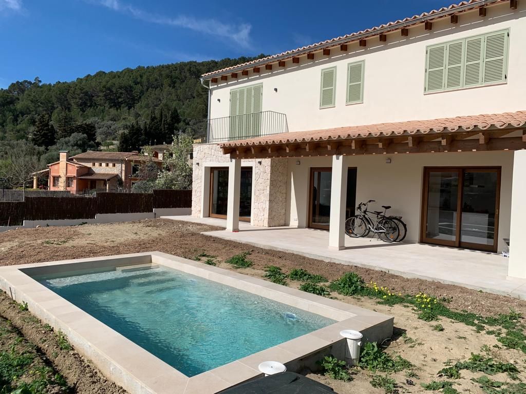 Casa con patio y piscina en un soleado jardín trasero, con bicicletas guardadas bajo una terraza cubierta.