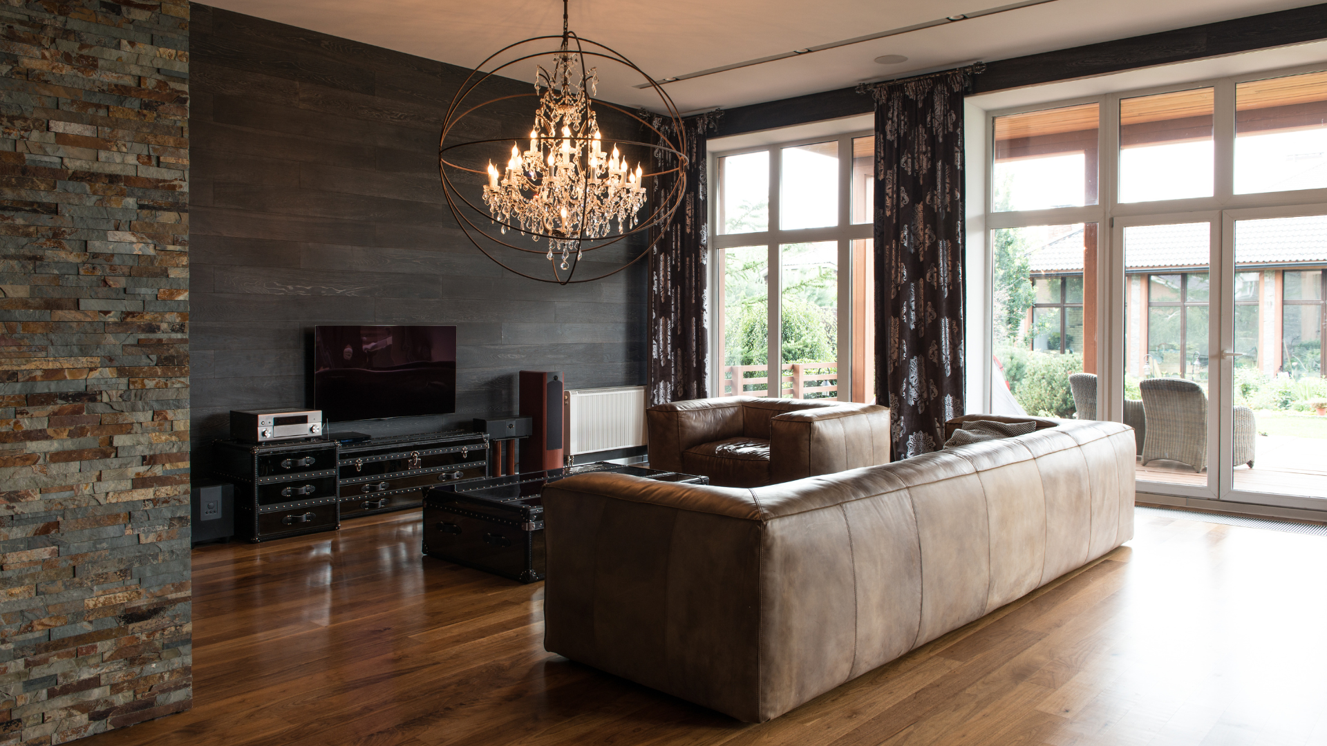 Living room with brown leather sofa, chandelier, and large windows.