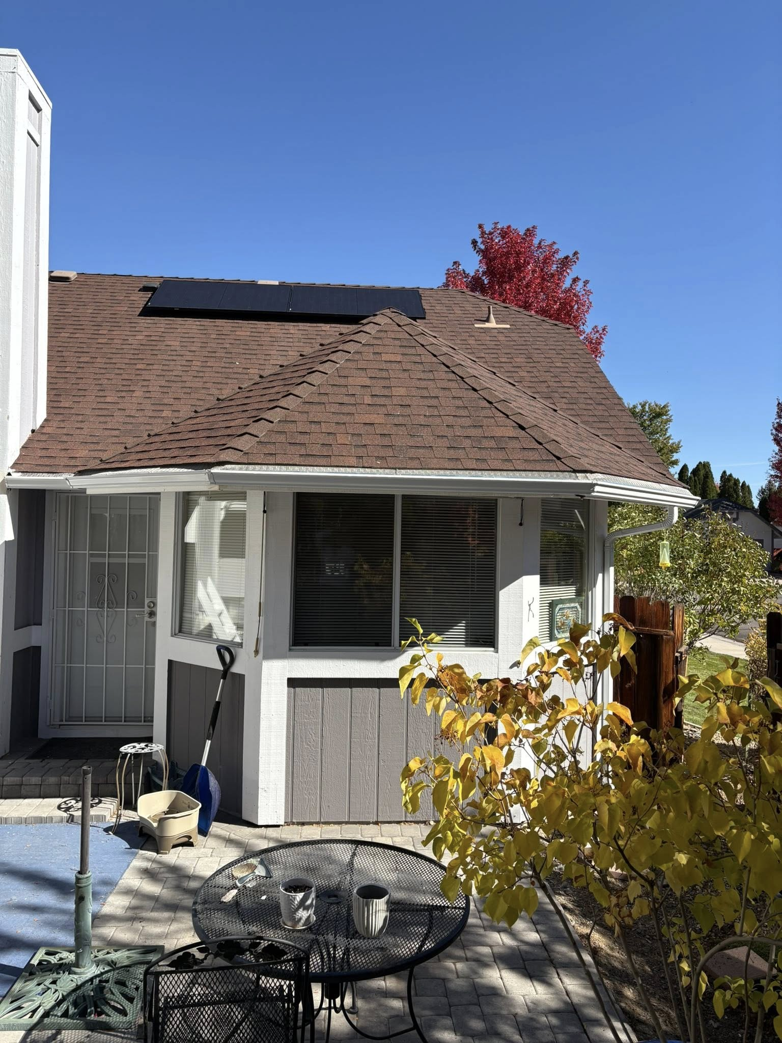A house with solar panels on the roof, a patio, and a table. Blue sky and autumn colors.