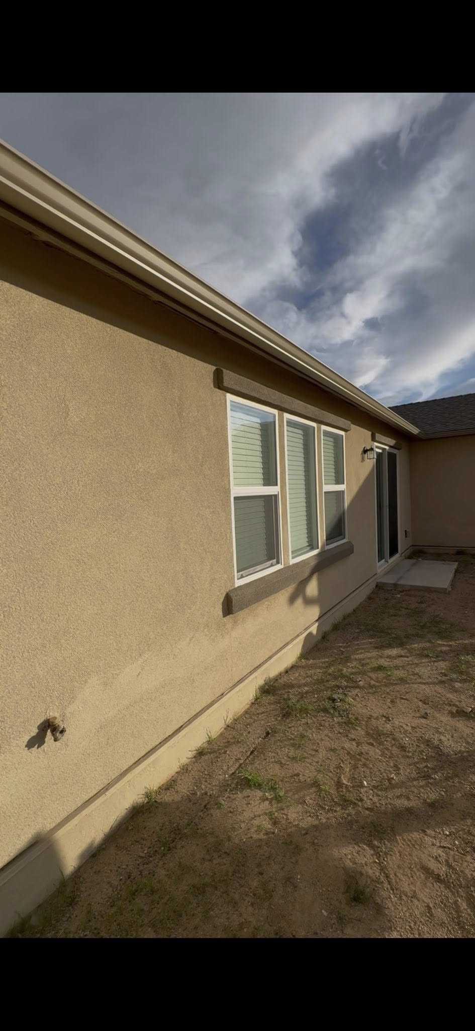 A beige stucco house exterior with windows, a door, and a brown lawn under a cloudy sky.