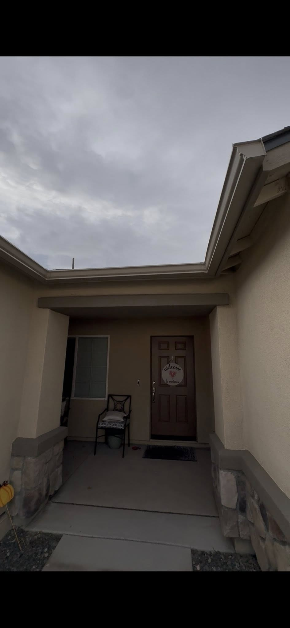 A covered entryway of a home. A door and a window are visible. The sky is overcast.