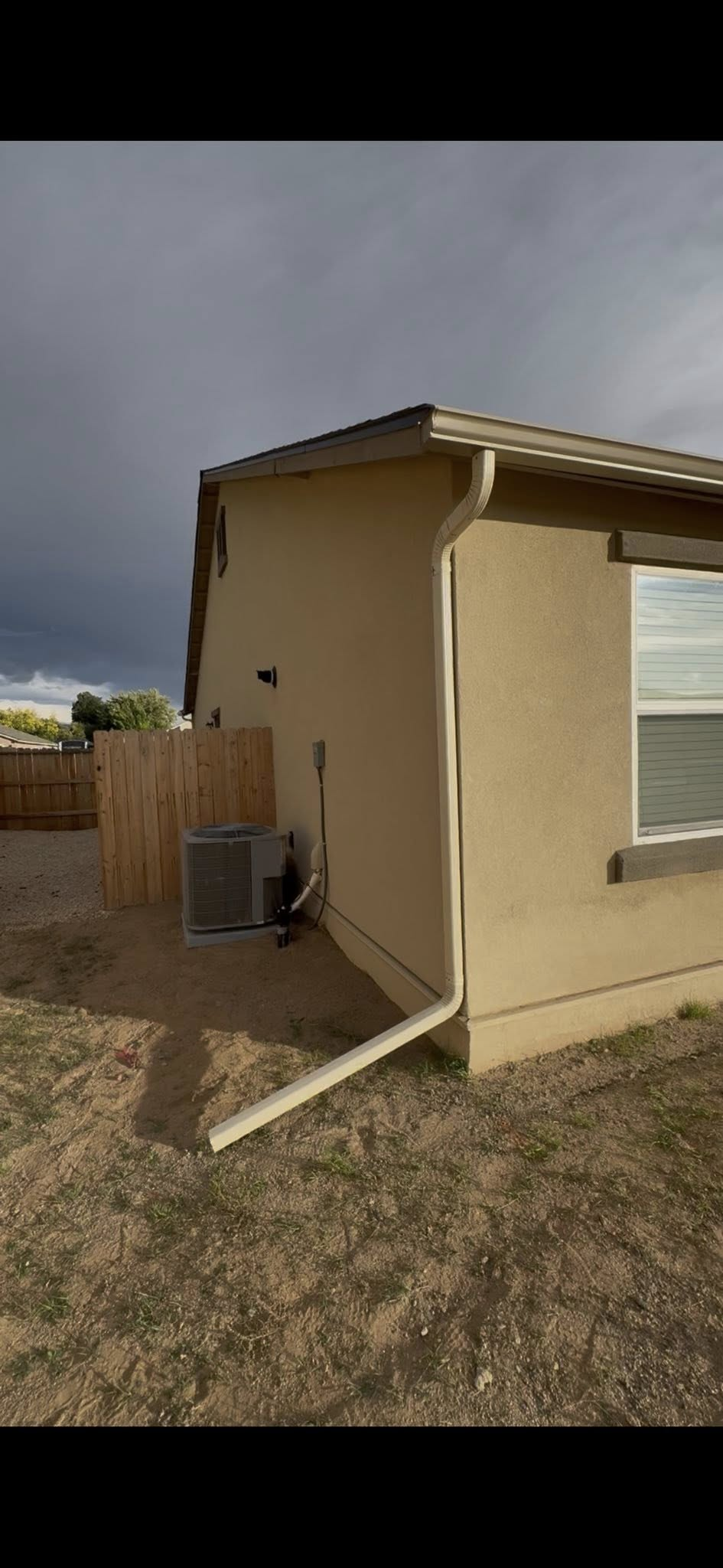 Beige house exterior with an air conditioning unit and a fence, with a cloudy sky in the background.