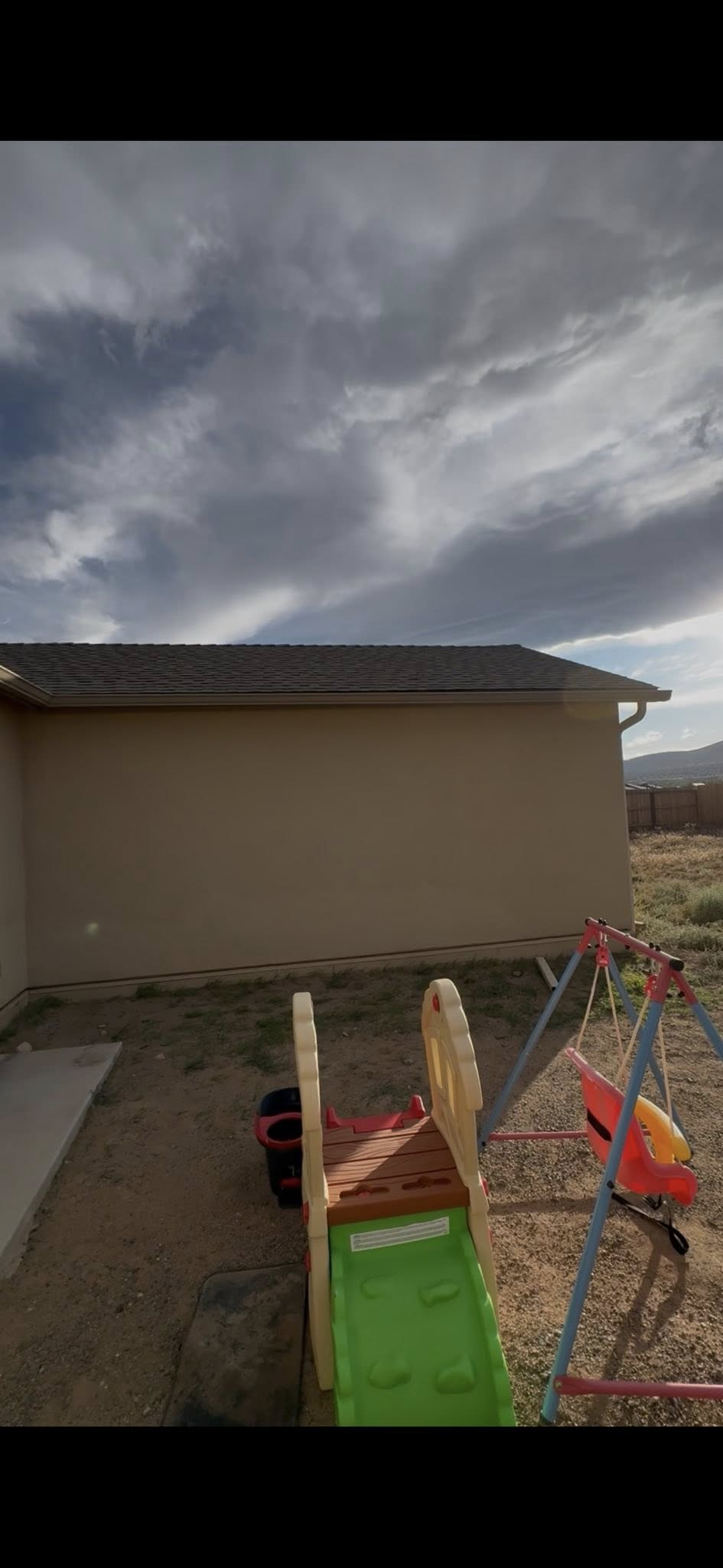 Exterior view of a beige building with a dark roof, a playground, and cloudy sky.