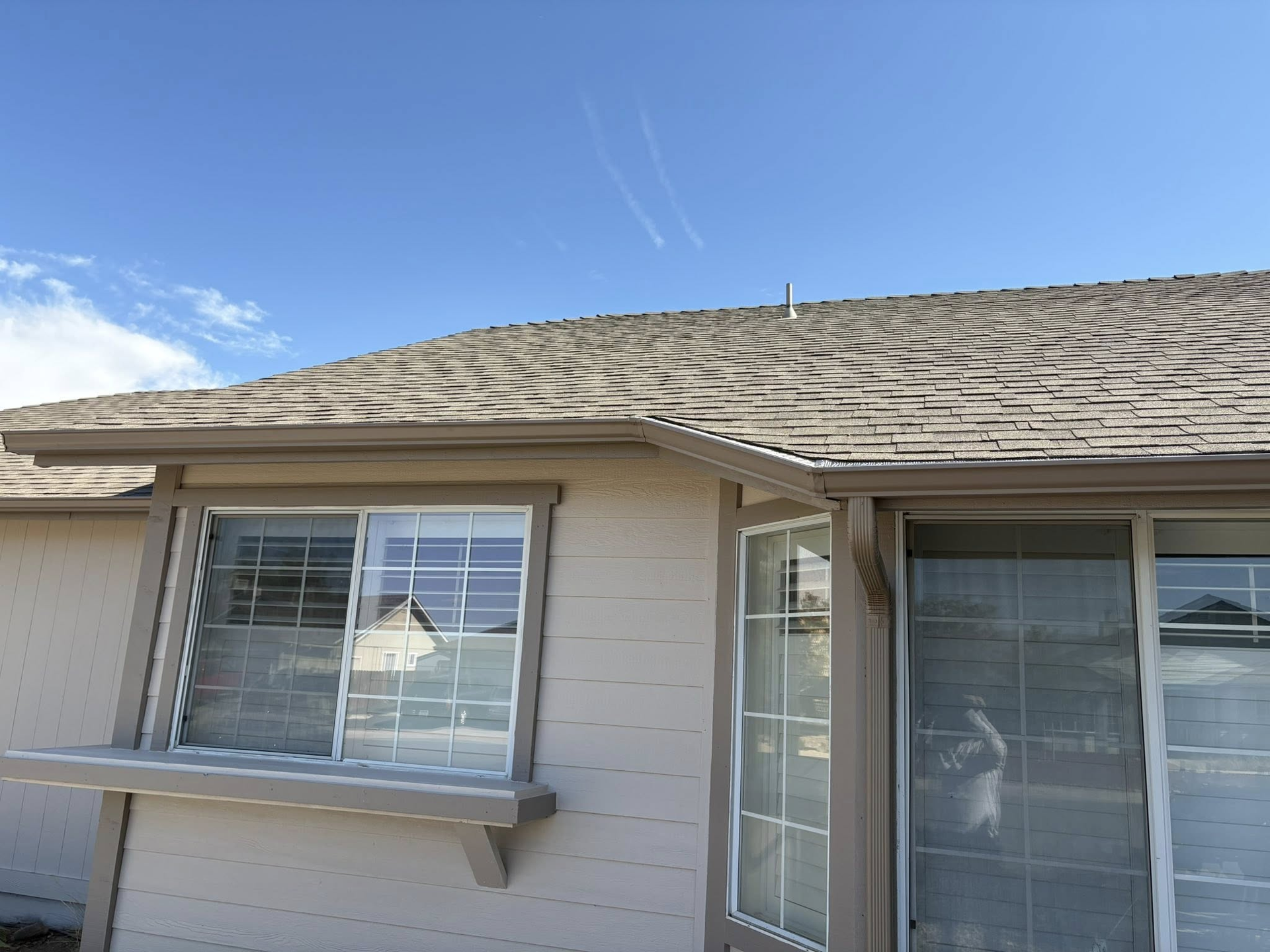 Exterior view of a beige house with a brown roof and windows on a sunny day.