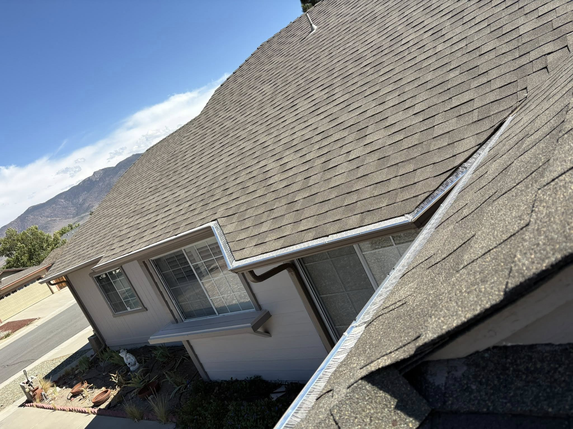 Gray shingled roof of a house with white trim, against a blue sky with mountain in the background.