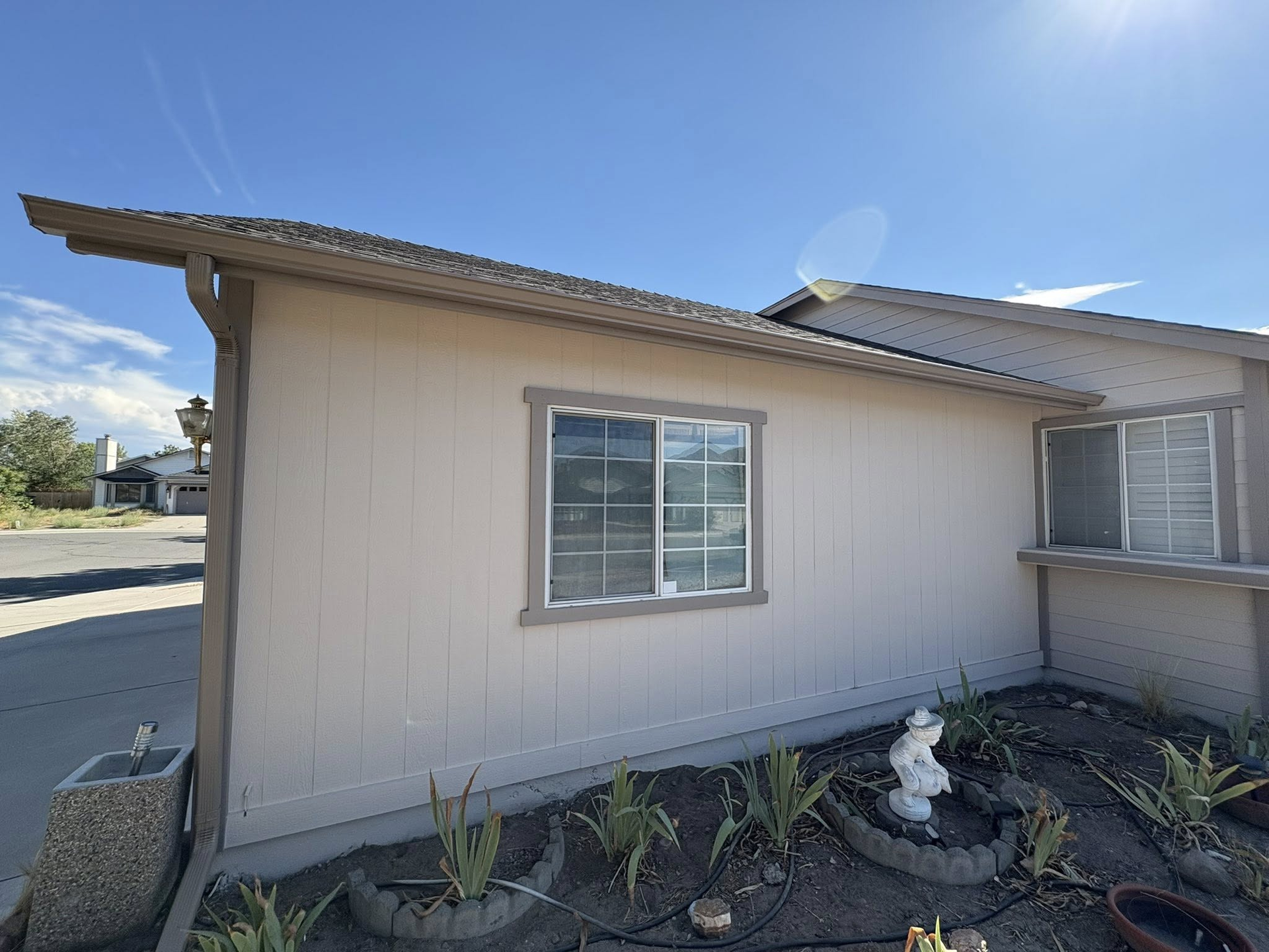 Beige house exterior with a window, under a blue sky, and a small garden in front.