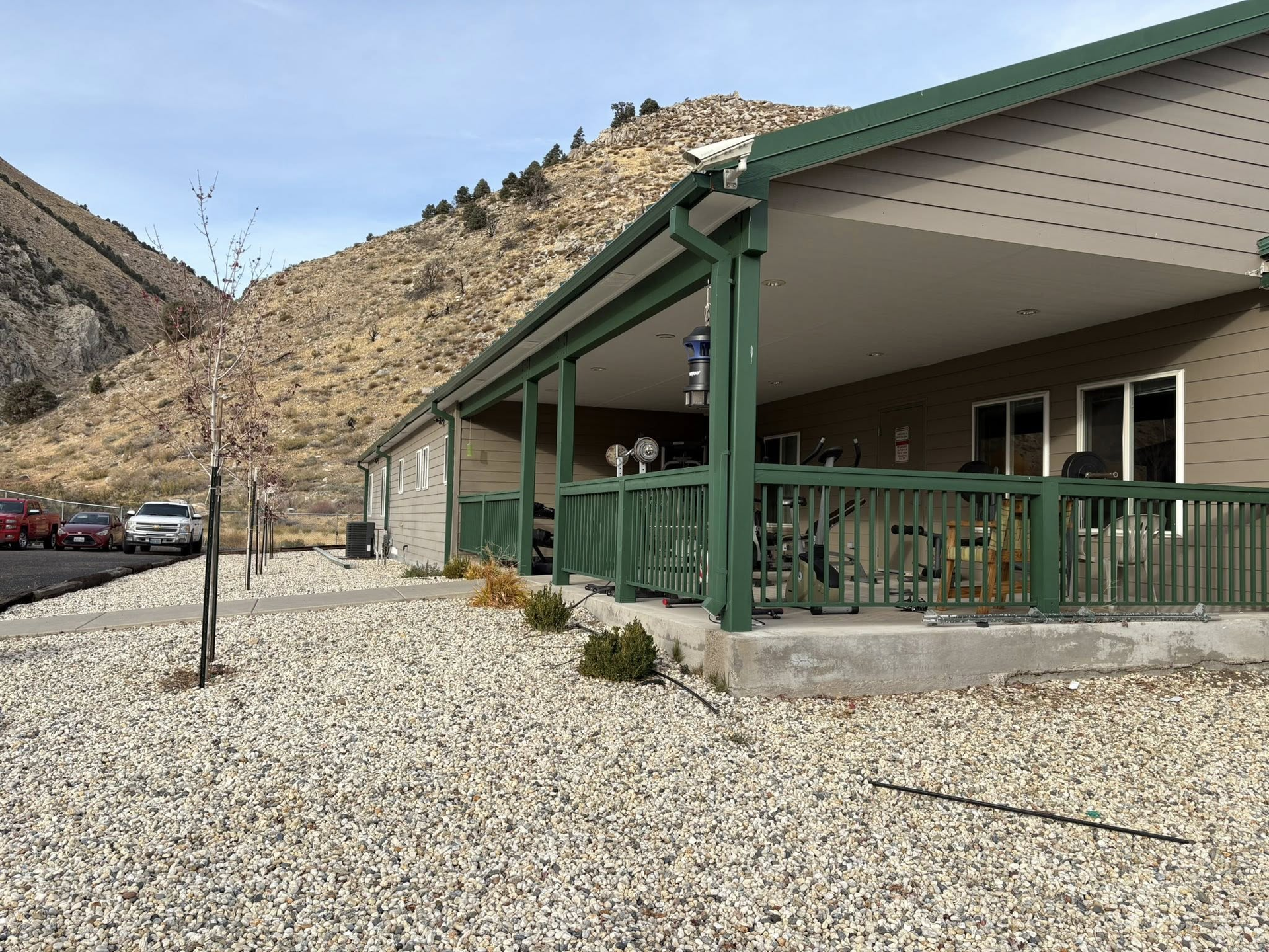 Building with green trim and covered porch; gravel and mountain backdrop.
