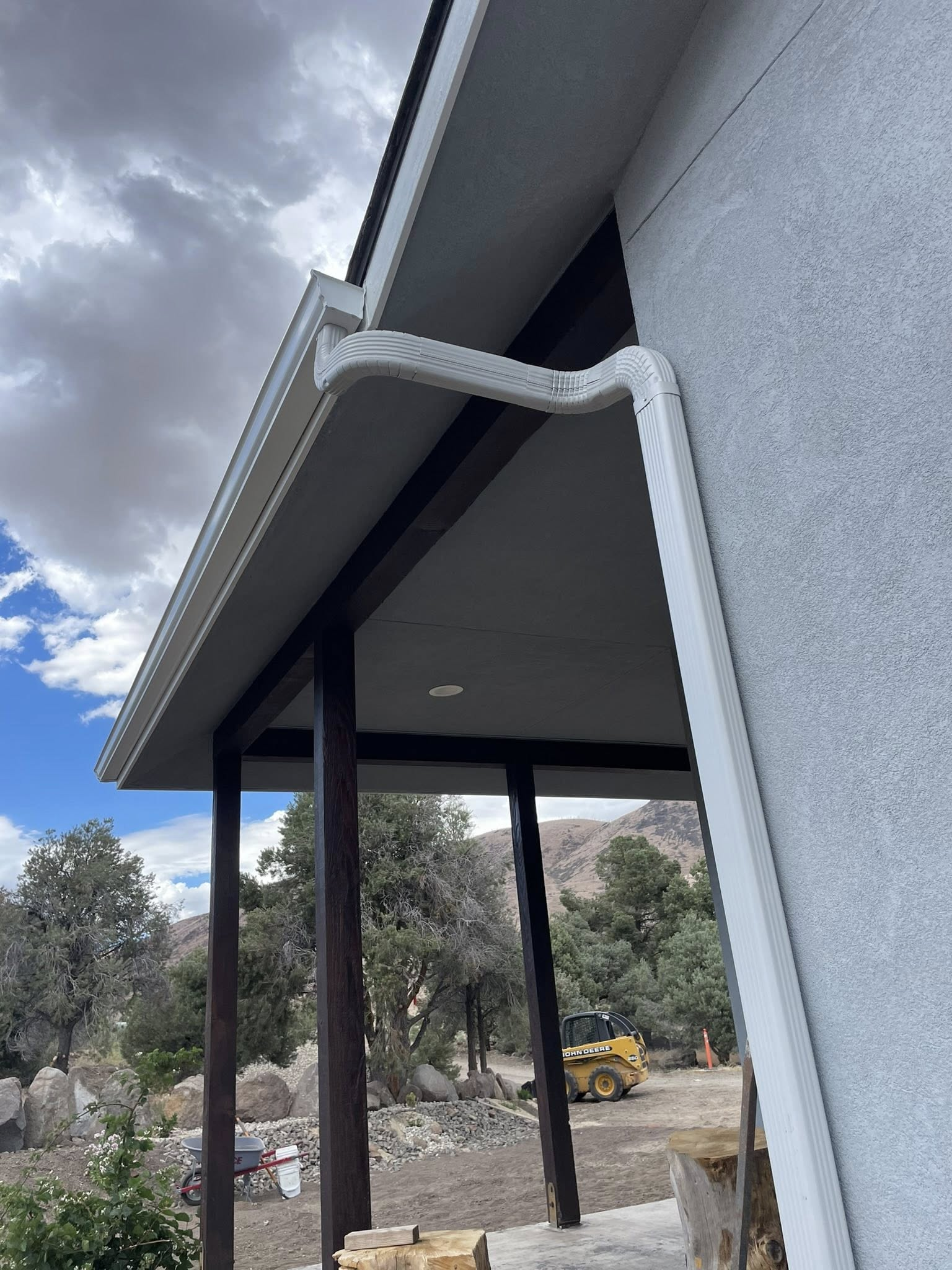White gutters on a house with a porch and dark columns. Cloudy sky and mountains in the background.