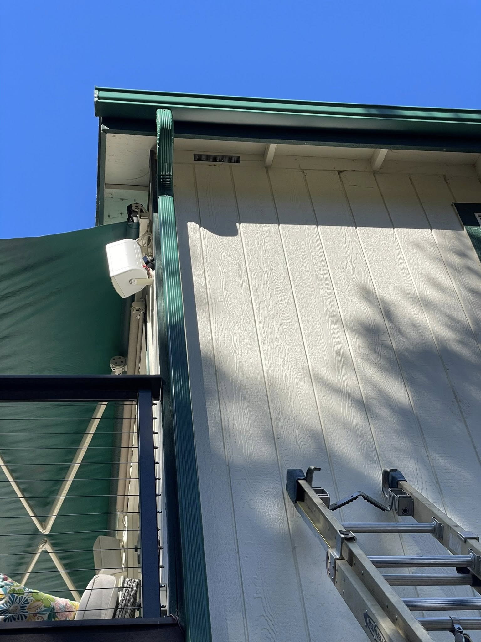 White device mounted on green awning next to a building with a ladder.