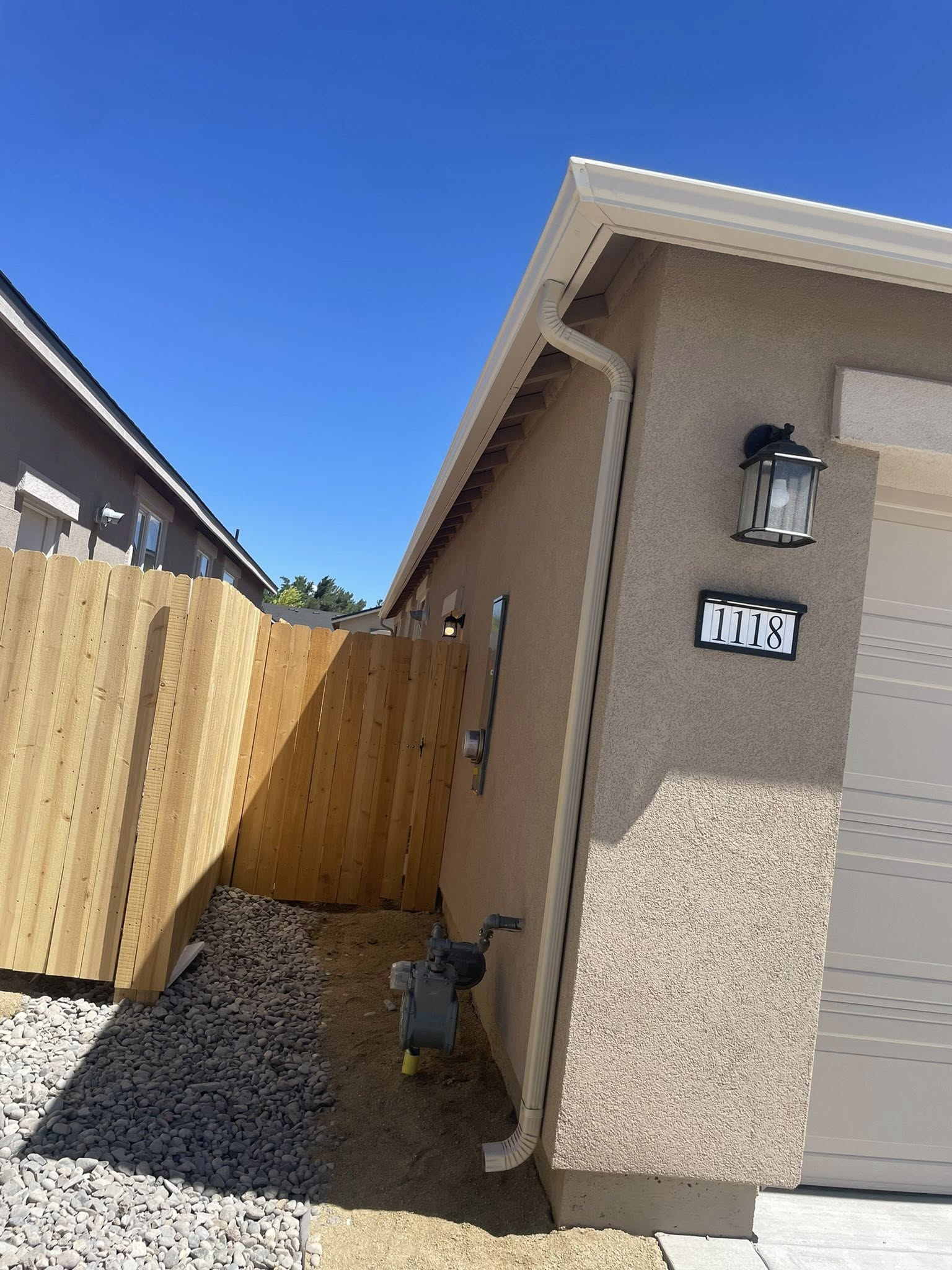 Side of a stucco house with white trim, a fence, and a clear blue sky.