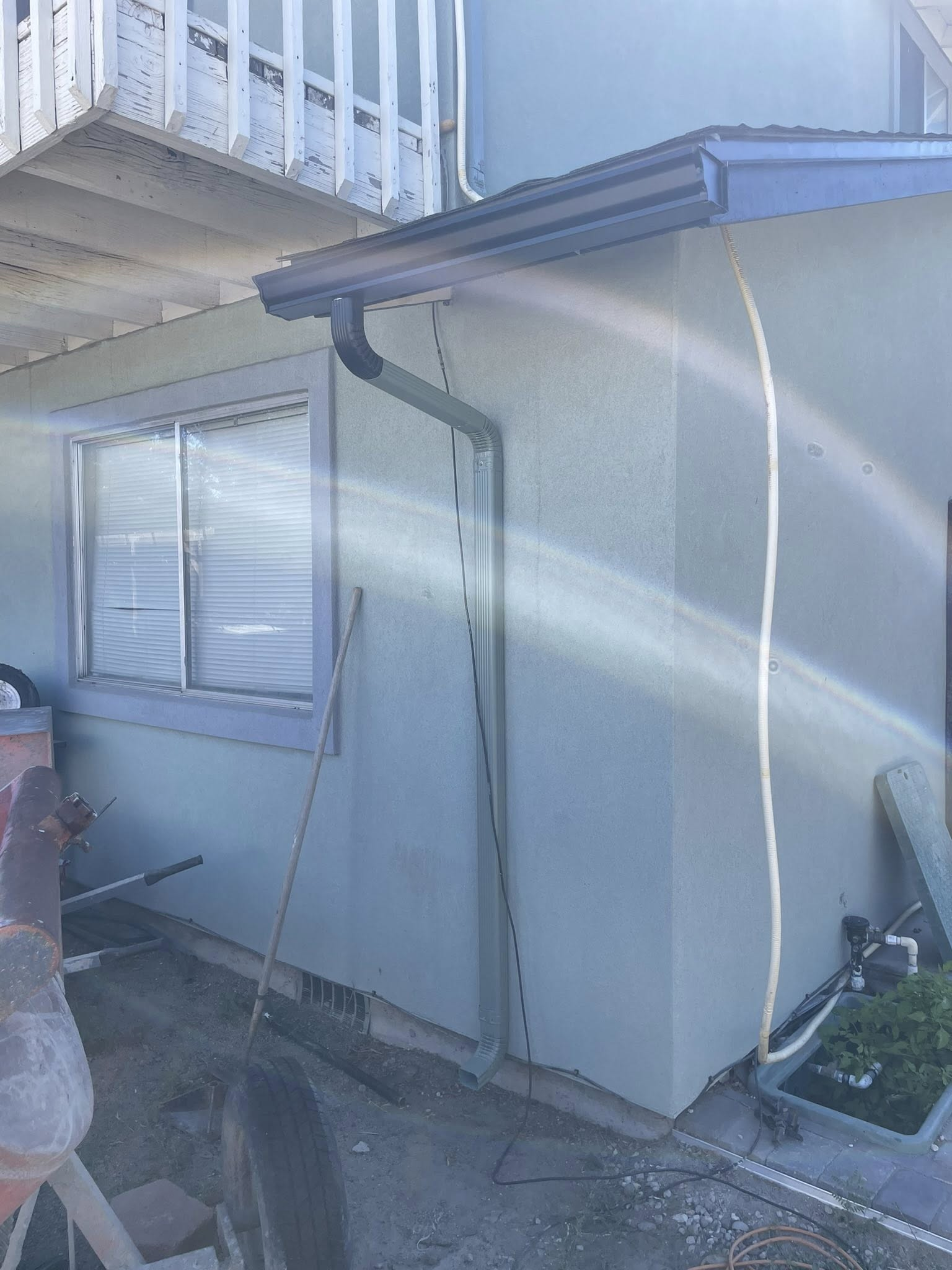 Light blue stucco building with a gutter and window. A white cable runs down the wall.