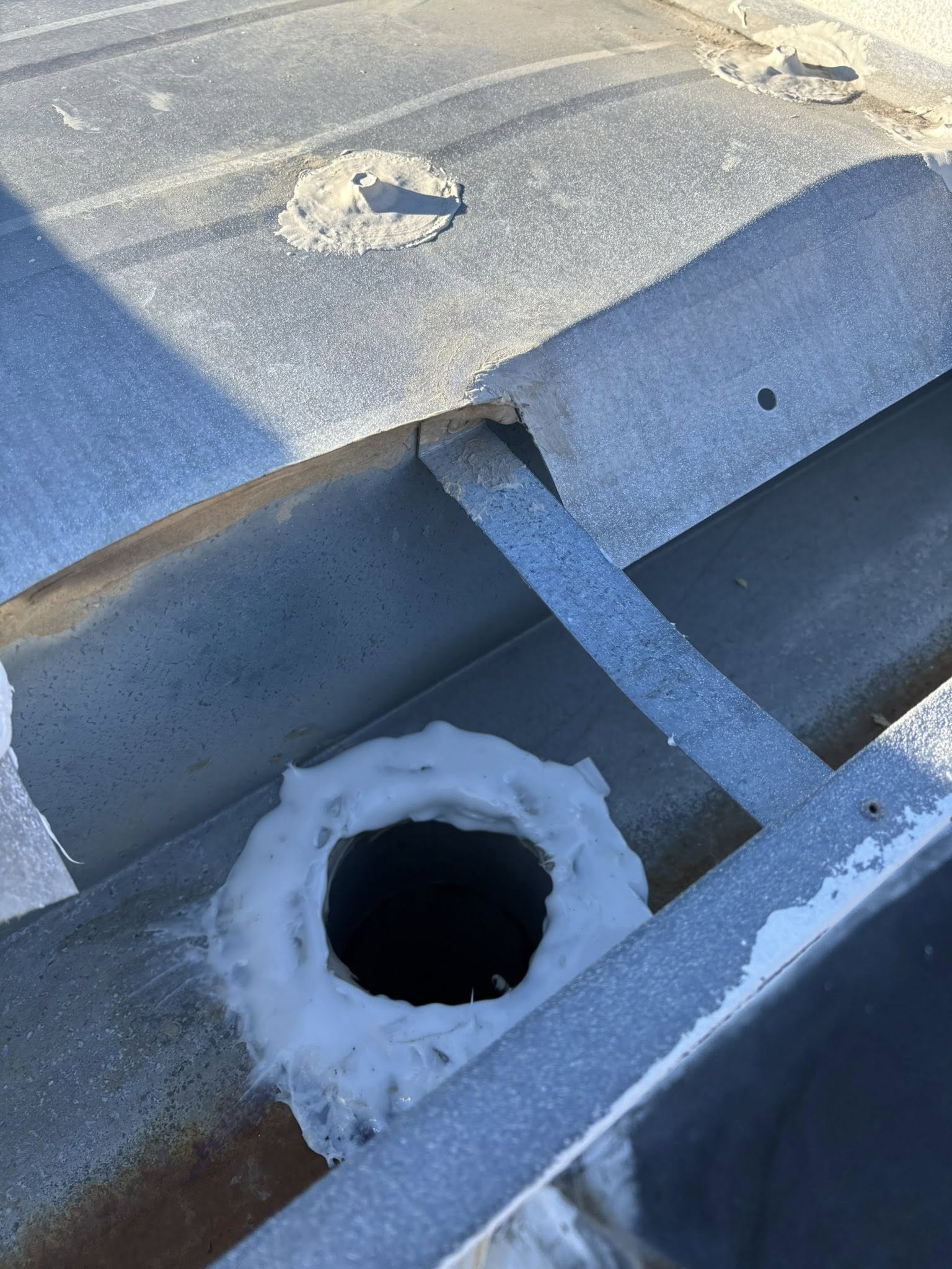 A metal roof drain with ice buildup around the opening, in a channel.