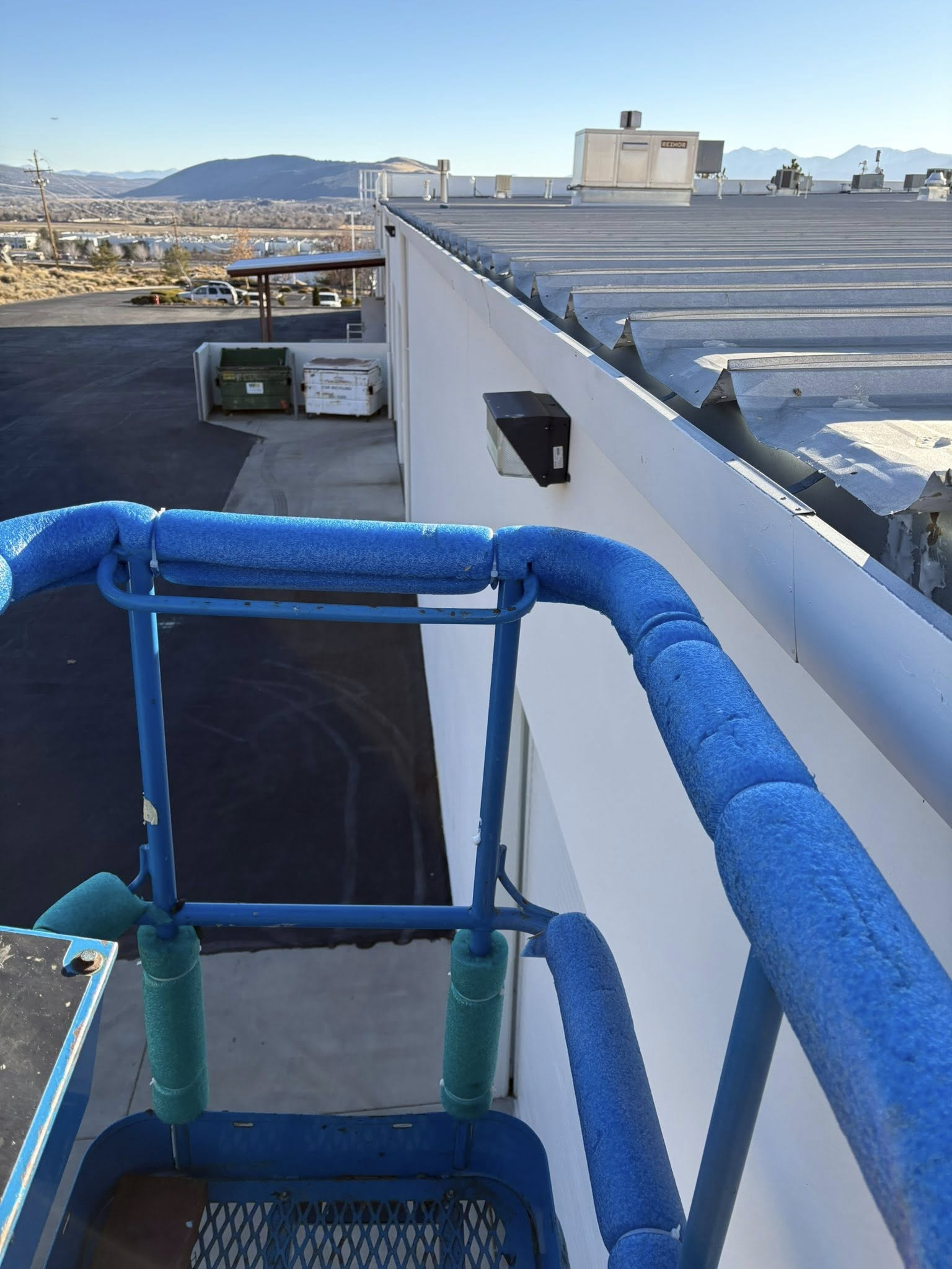Blue aerial lift platform near a white building with mountains in the background.