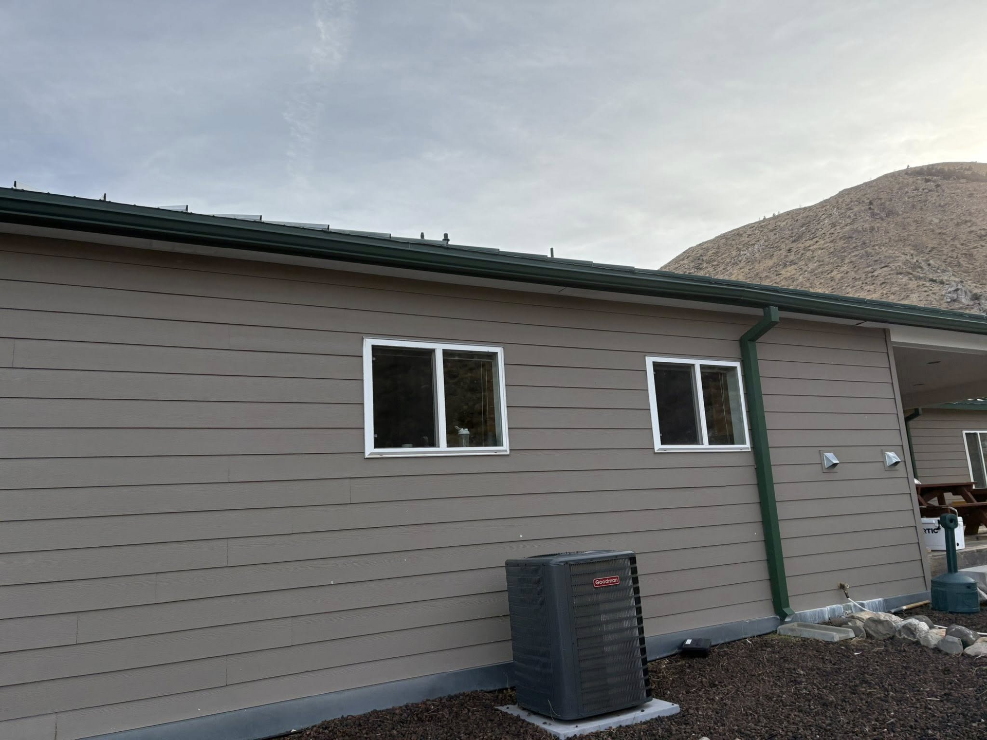 Beige-sided building with white-framed windows, green trim, and an air conditioning unit. Mountain in the background.
