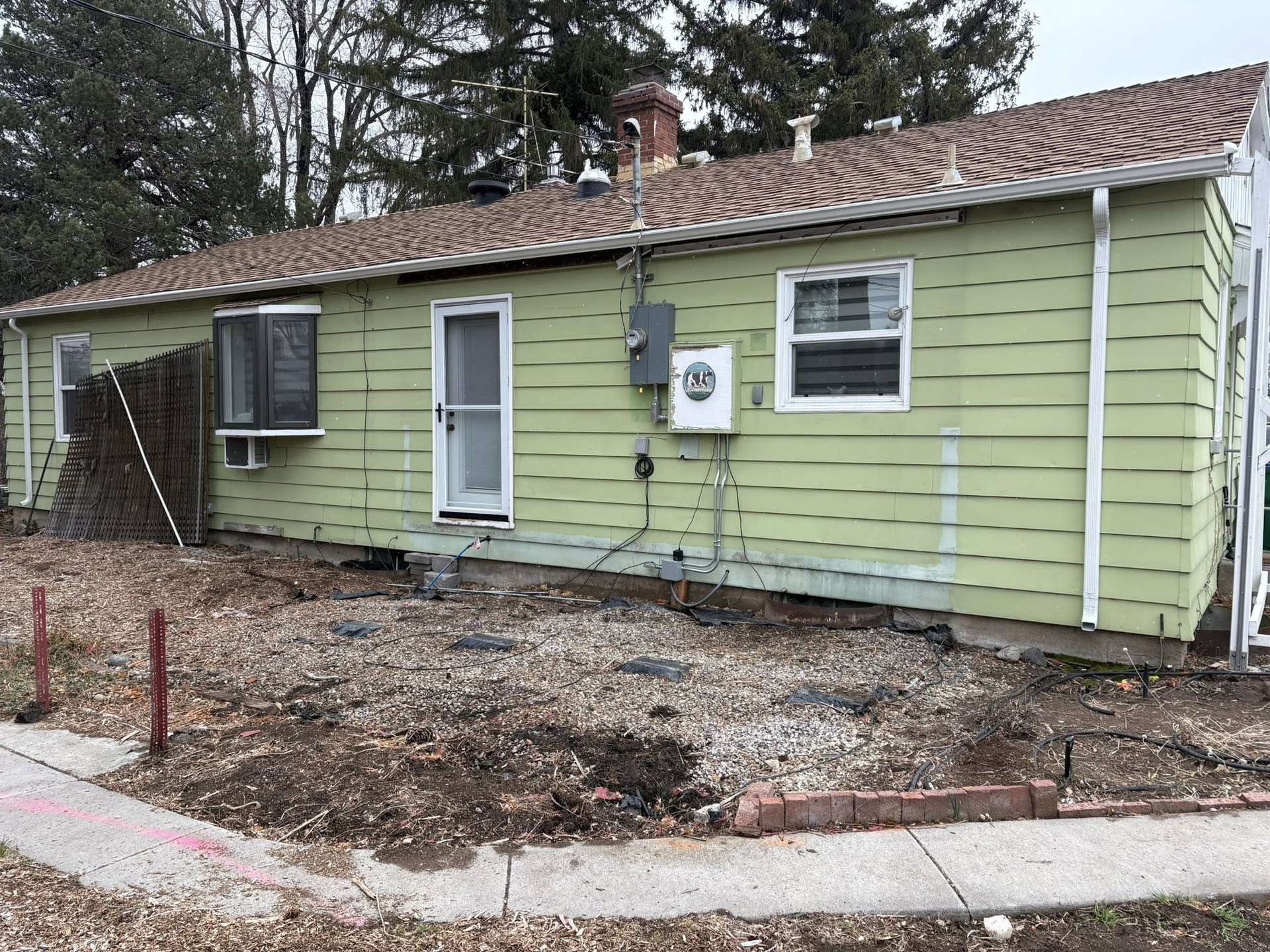 Green house with a brown roof and bare dirt yard.