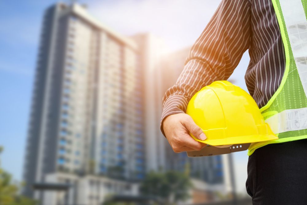 A Construction Worker Is Holding a Yellow Hard Hat in Front of A Building Under Construction — Iconic Construction Industries in Garbutt, QLD