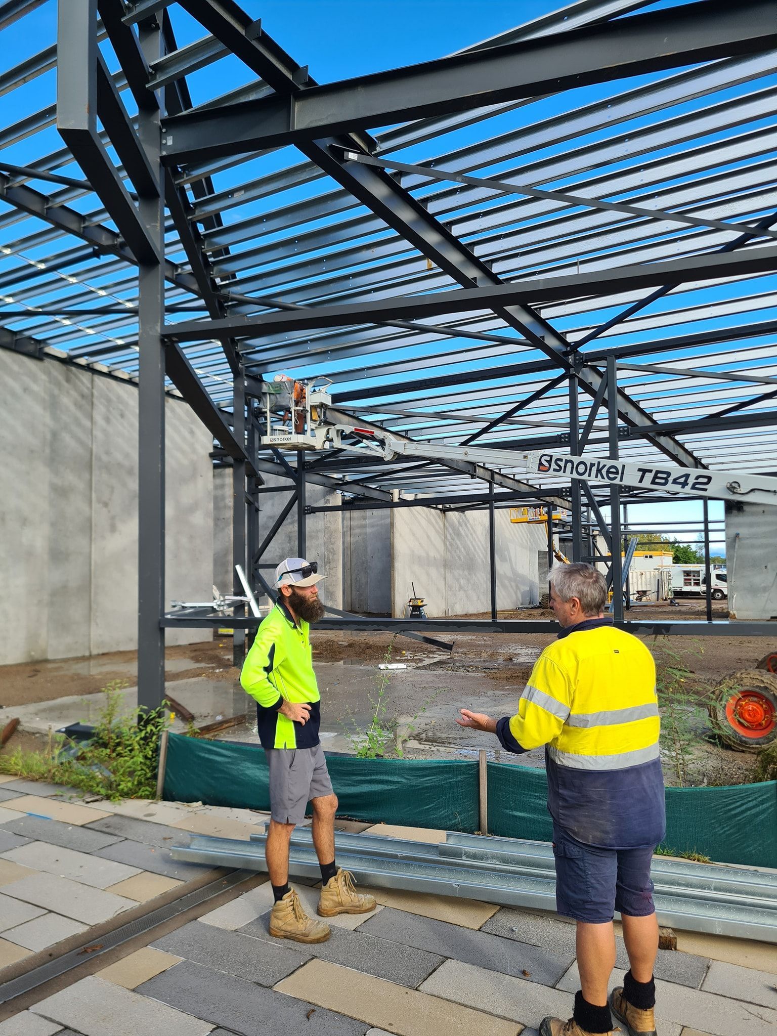 A Man Is Holding an Orange Hard Hat in Front of A Construction Site — Iconic Construction Industries in Garbutt, QLD