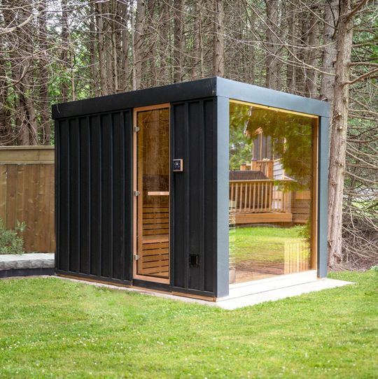 A black shed with a glass door is sitting in the middle of a lush green field.