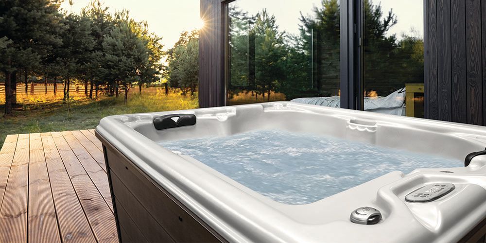 A hot tub is sitting on a wooden deck next to a window.