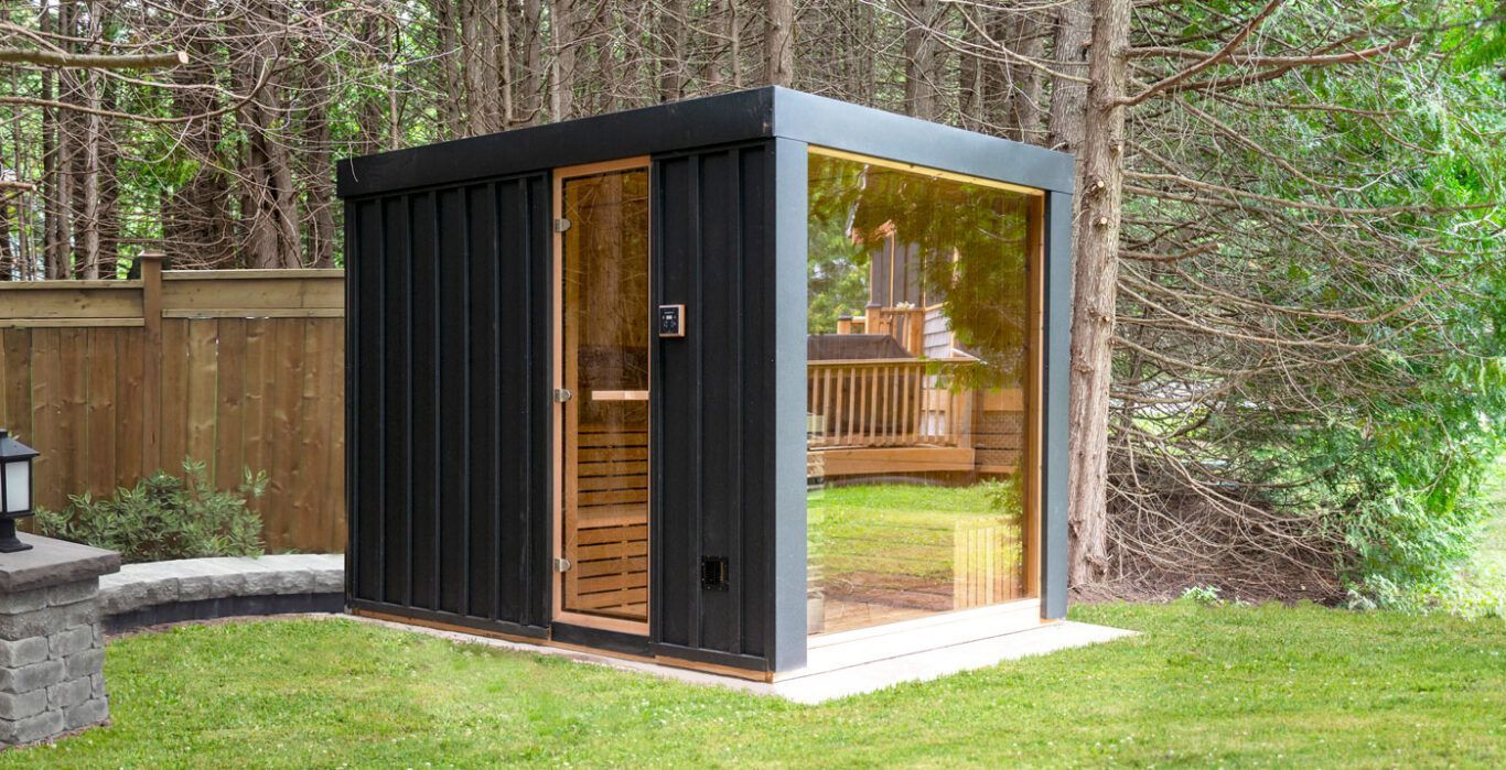 A black sauna is sitting in the middle of a lush green yard.