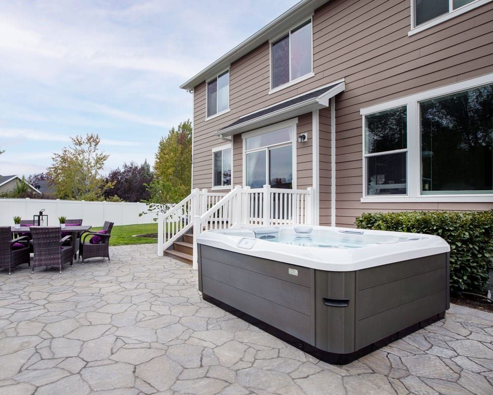 A hot tub is sitting on a patio in front of a house.