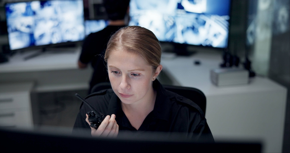 A woman is sitting in front of a computer talking on a walkie talkie.