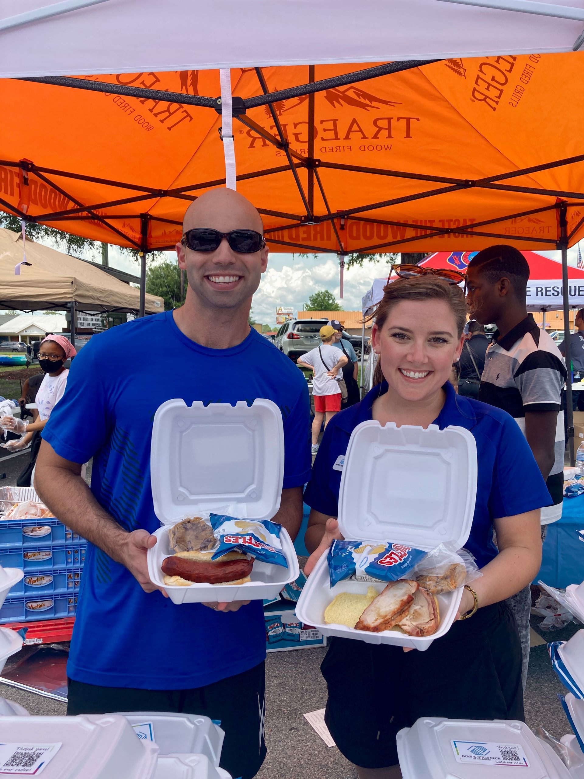 Two people in blue shirts holding food containers under an orange tent.