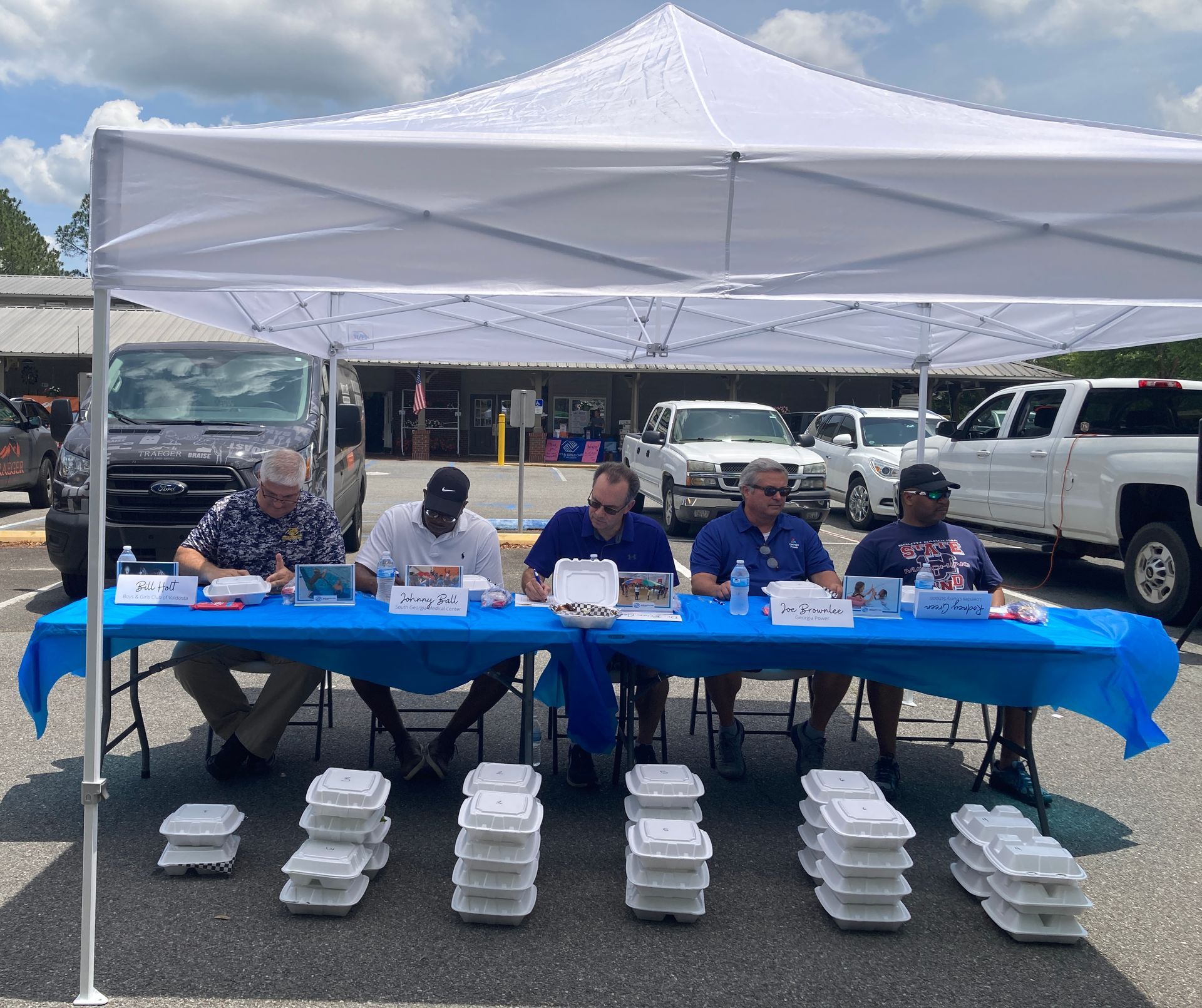 Five people seated at a table under a tent, judging BBQ cook-off