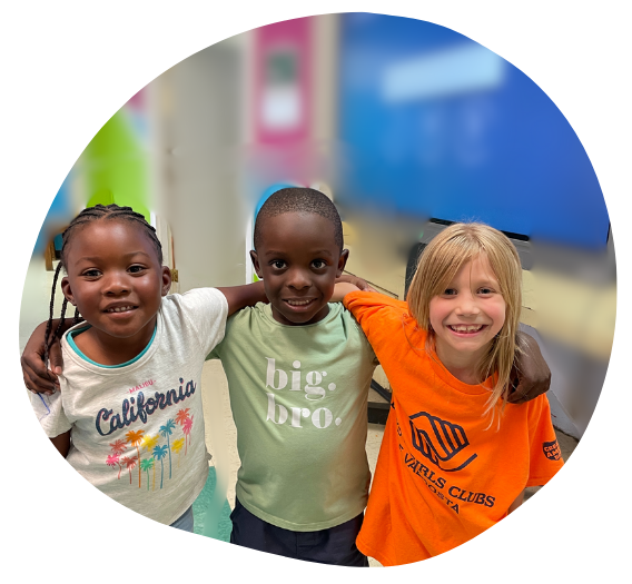 Three smiling children with arms around each other. They are indoors with a blurry background at the Echols County location.