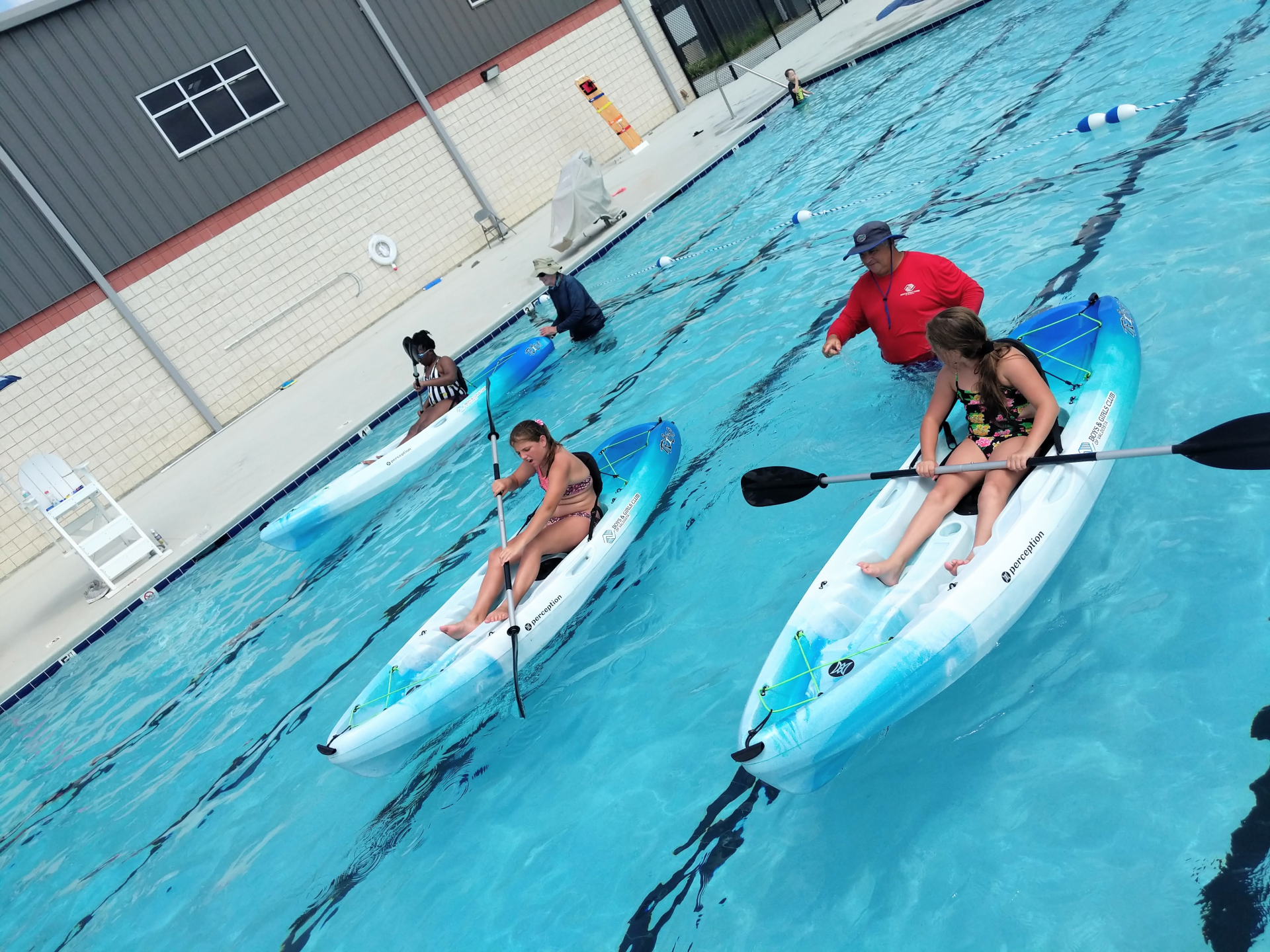 Students kayaking in a pool with an instructor. Blue and white kayaks, with clear water.