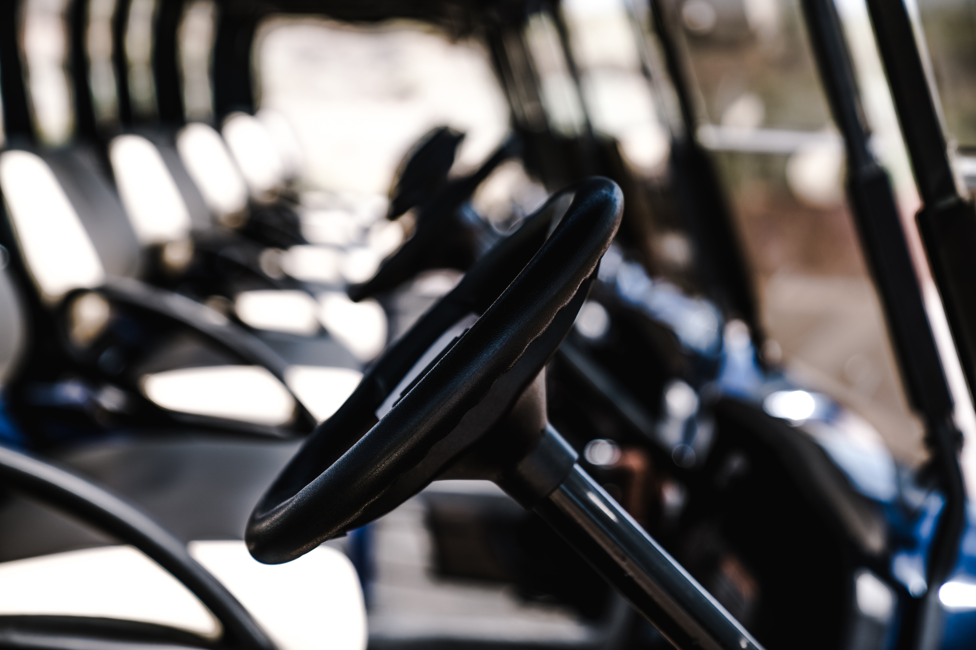 Black steering wheel in a golf cart, with rows of white and black seats.