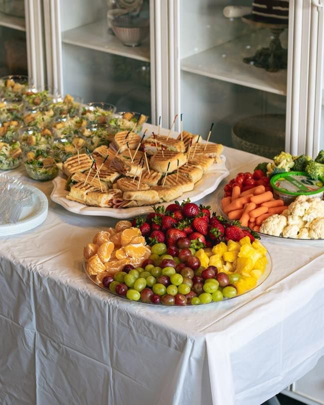 Table spread of party food: sandwiches, fruit platter, veggie tray, and salad.