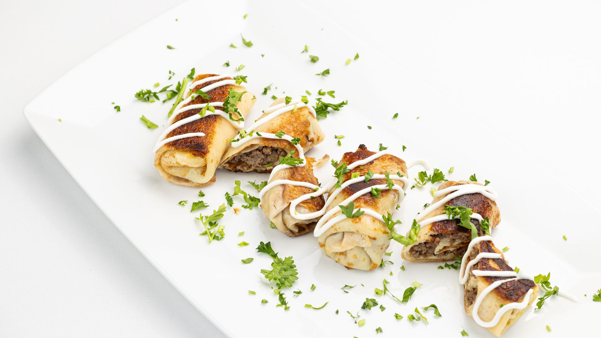 Plate of fried appetizers, drizzled with white sauce, garnished with parsley.