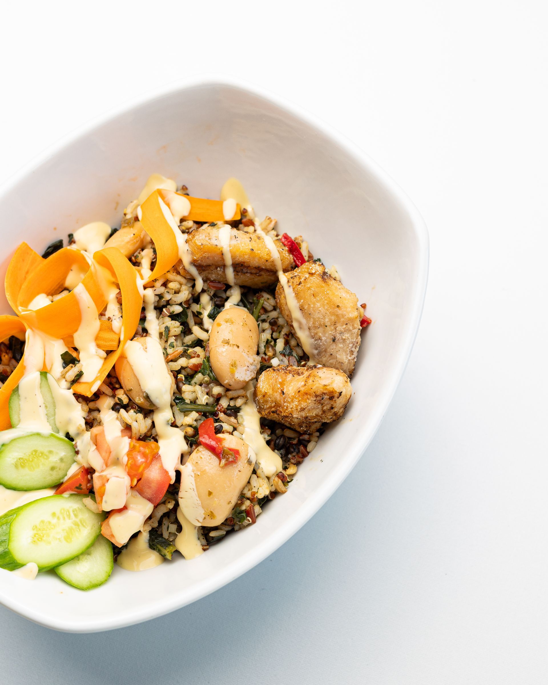 Bowl of food with vegetables, grain, and sauce, on white.