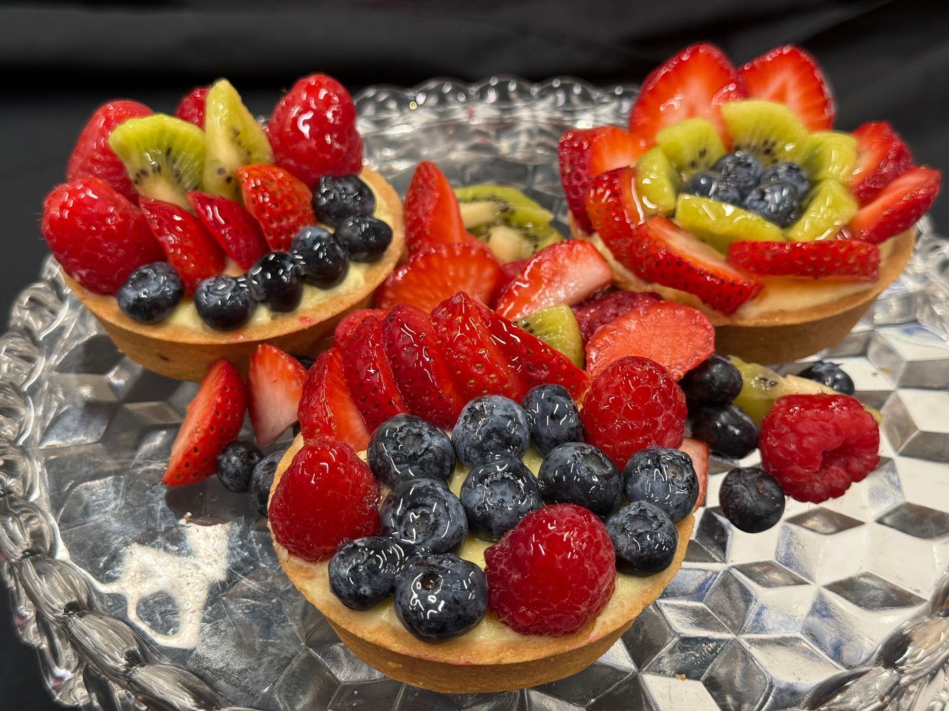Fruit tarts with strawberries, kiwi, and blueberries on a glass platter.