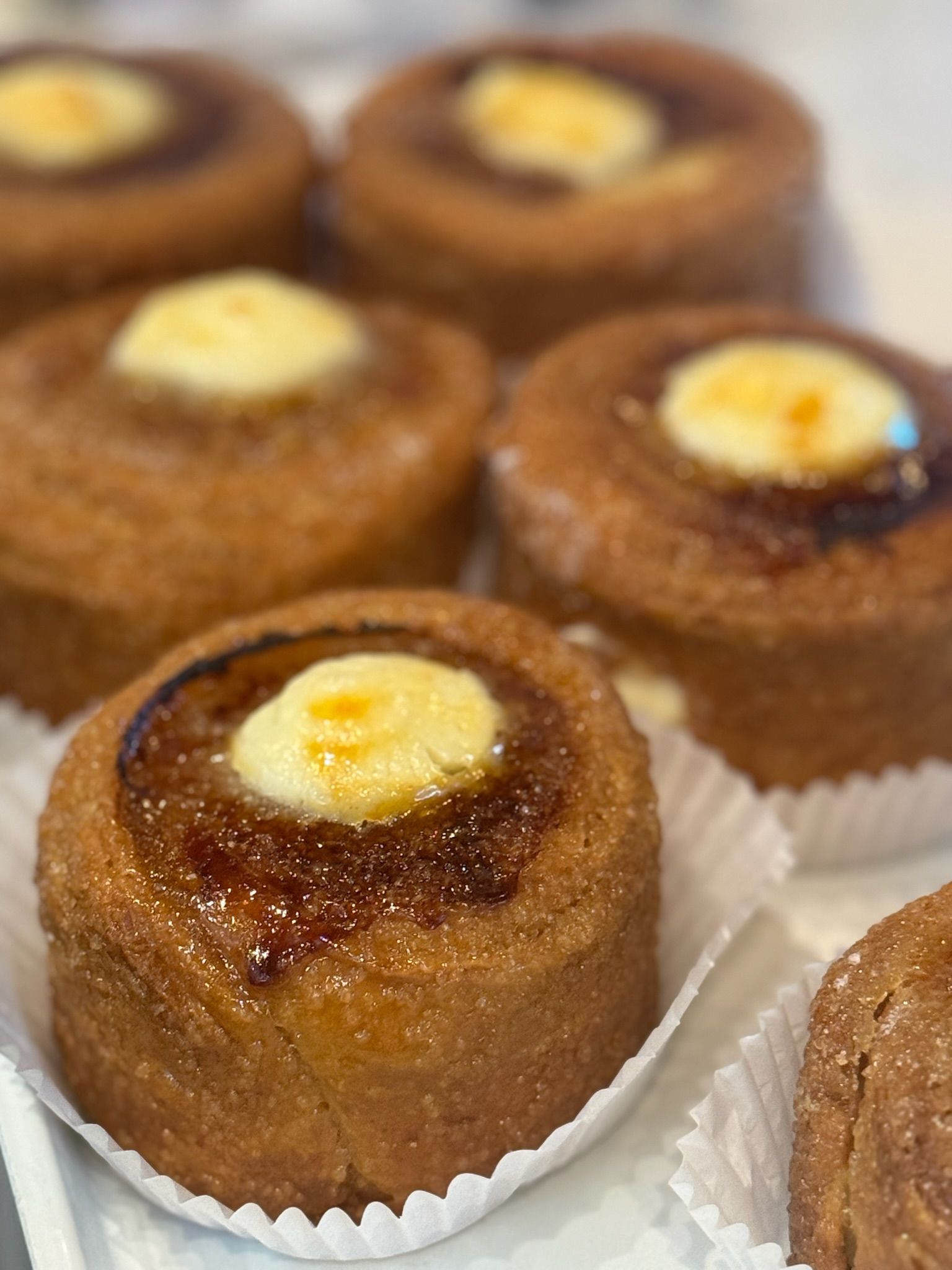 Close-up of several caramelized pastries with a cream topping, arranged in a white container.