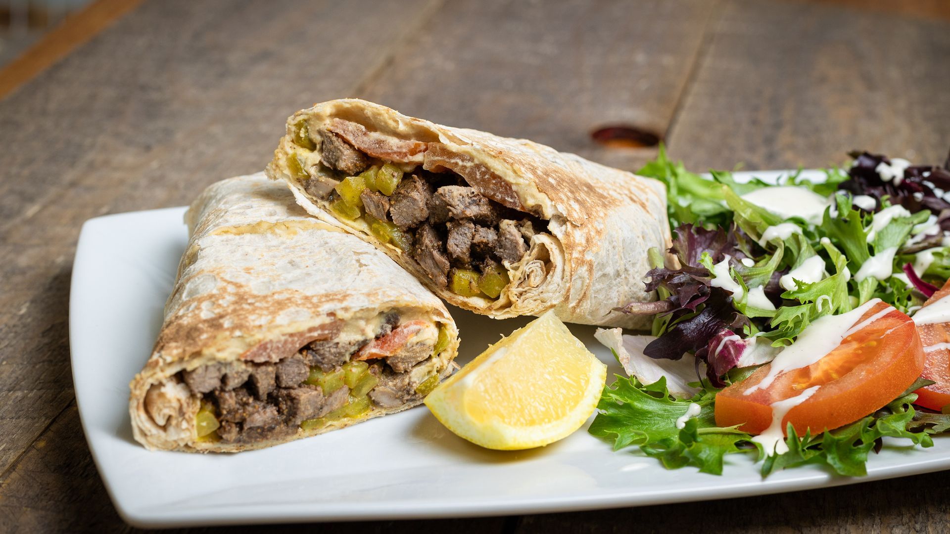 Sliced gyro wrap with a side salad and lemon wedge on a white plate.